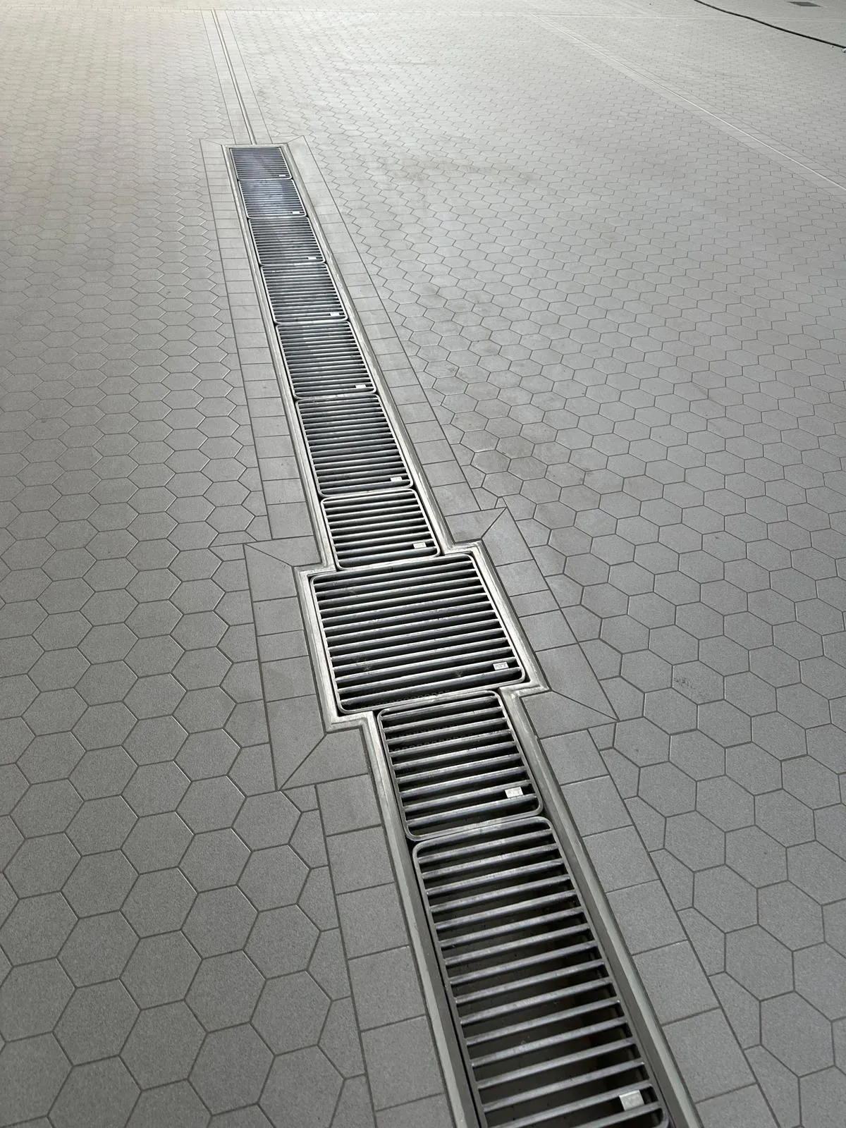 Detailaufnahme einer Edelstahl-Entwässerungsrinne mit Rost, eingefasst in Sechskant-Keramikfliesen